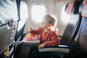 Preschooler girl eating snacks from lunch box while travelling by plane