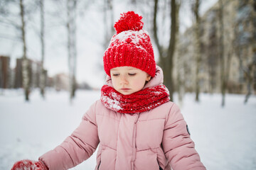 Adorable preschooler girl having fun in beautiful winter park on a snowy cold winter day