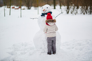 Adorable preschooler girl building a snowman on a day with heavy snowfall