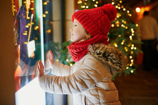 Preschooler girl looking at window glass of large department store decorated for Christmas