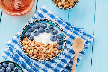 Bowl of granola with fresh blueberry and yogurt on a blue napkin. Breakfast with granola, berries and honey on blue boards. Healthy food. Top view