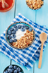 Bowl of granola with fresh blueberry and yogurt on a blue napkin. Breakfast with granola, berries and honey on blue boards. Healthy food. Top view