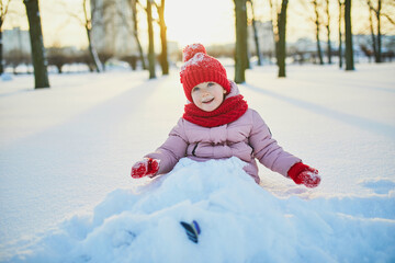 Adorable preschooler girl having fun in beautiful winter park on a snowy cold winter day