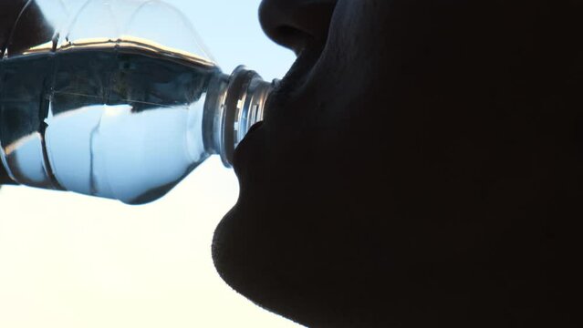 Silhouette of a man drinking water from a plastic bottle, close-up