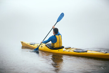 One man paddling kayak at autumn misty river at foggy autumn morning.