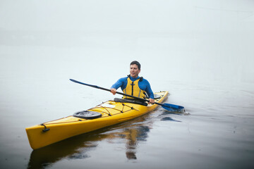 Obraz premium One man paddling kayak at autumn misty river at foggy autumn morning.
