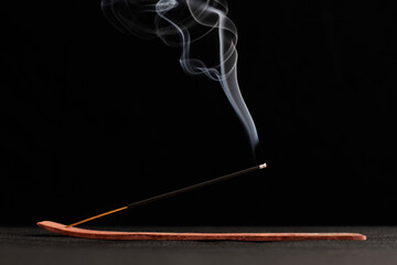 Smoke curls of burning incense stick in wooden holder for relaxation and meditation black background