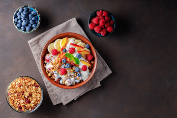 Yogurt with granola, berries, fruits and fresh mint. Plate with a healthy breakfast and ingredients on a dark background. Top view. Copy space