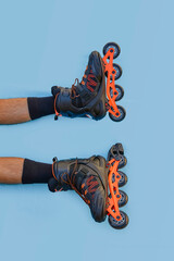 Vertical photo of two legs of boy with inline skates on blue background with copyspace