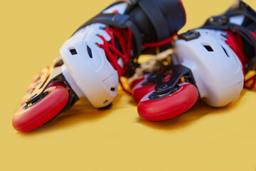 Close-up of the toe of a pair of inline skates one on top of the other on a yellow background with...