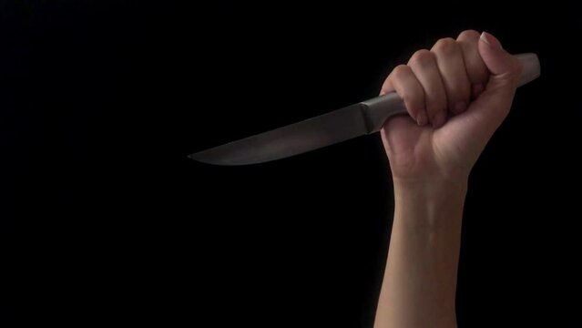 Human hand with knife shot on a black background. Woman's hand holds knife. The hand makes stabs with a knife. Concept of violence, murder with kitchen knife