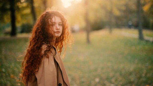 Gorgeous young ginger woman turn around with flying hair the sunset in the park. Flirting red head smiling woman walking alone.
