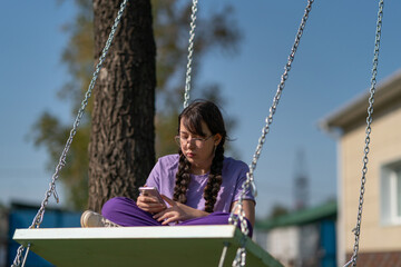 person sitting on a swing with phone in the hands