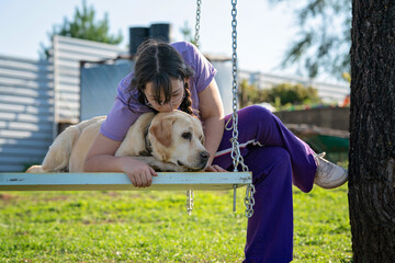 A teenage girl swings on a swing with her old Labrador dog. Girl playing with her dog