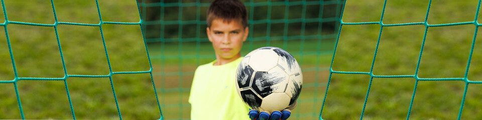 Banner 1x4 with young football goalkeeper in the gate in bokeh holds a caught ball