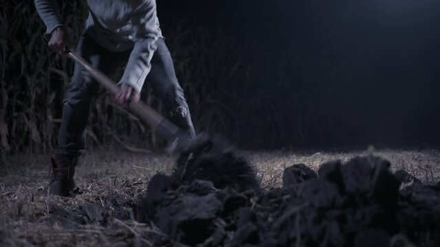 Killer digs grave at night. Young scary man digs hole in field. Close up of legs.
