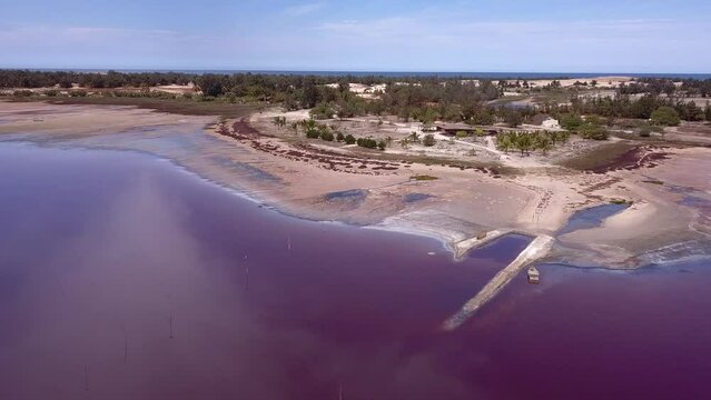 Aerial footage of pink lake full of salt with dry shore, clouds reflecting on the lake and ocean in background, Retba lake, Dakar, Senegal, going sideway along shore while panning.