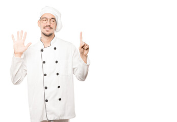 Happy young chef doing a number six gesture with his hands