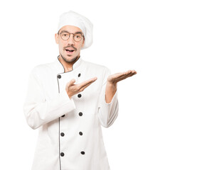 Surprised young chef holding something with his hand