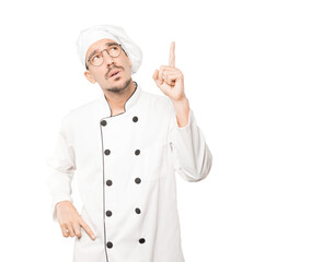 Hesitant young chef pointing up with his finger