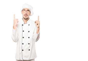 Hesitant young chef pointing up with his finger