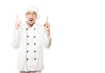 Amazed young chef pointing up with his finger