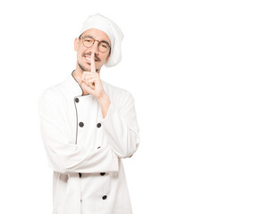 Happy young chef asking for silence gesturing with his finger