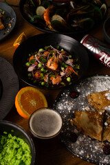 Table with many plates of food. Lamb ribs, mussels, french fries, aspic, fried pork. Table served