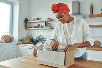 Curious African woman unpacking box while standing at the domestic kitchen