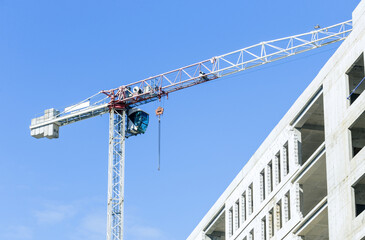 Construction site. A construction crane and a building under construction against a blue sky background. A construction crane is working, the walls of buildings are being erected.