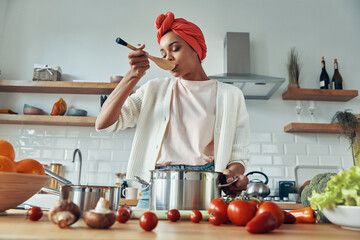 Confident African woman mixing something in pan and smiling while preparing food at the kitchen