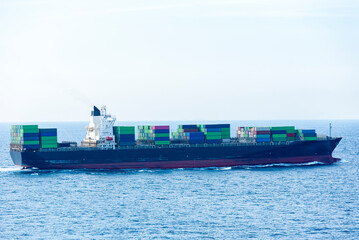 Container ship sailing through the calm sea, she is fully loaded with cargo containers.