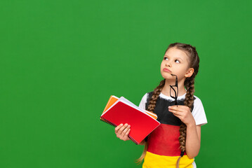 A thoughtful child with a German flag and a notebook in his hands on a green isolated background....