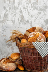 Homemade freshly baked bread, buns and a long loaf in a large wicker basket. Wood rustic table, board, ears, wheat, rye, grain harvest. Rural food cooking