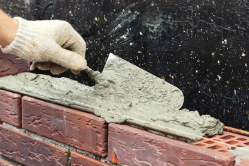 A worker builds a brick wall. Applying cement to brick. Hands in gloves and spatula. selective focus