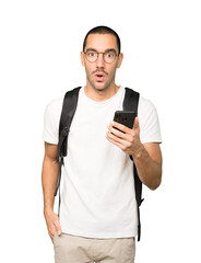 Surprised student pointing and using his mobile phone