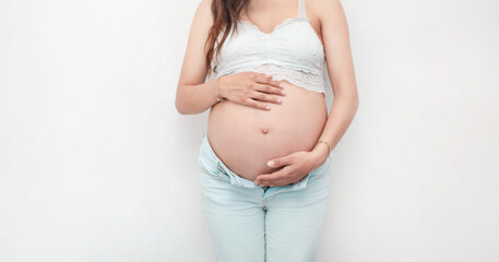 Fotografía de medio cuerpo de una mujer caucásica embarazada tocando su abdomen sobre un fondo...
