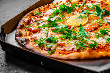 Pizza with Mozzarella cheese, salmon fish, tomato sauce, arugula, lemon. Italian pizza on Dark grey black slate background