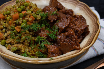 Vegan buckwheat and vegetables with seitan on plate, dark table, copy space