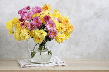 Yellow and pink chrysanthemums in a glass jug on the table. Bouquet of autumn flowers.