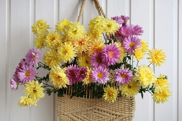 Garden chrysanthemums in a summer woven bag on the wall close-up.