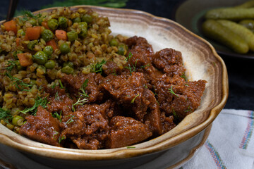 Vegan buckwheat and vegetables with seitan on plate, dark table, copy space