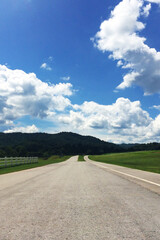 Mountains asphalt road through the green field and clouds on blue sky in summer day