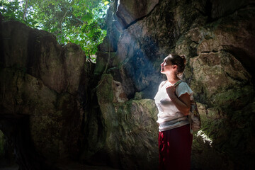 Mujer caminando por cavernas naturales y mirando hacia una filtración de luz que le alumbra la cara