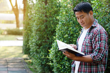 Asian man is at the park, holds book to read. Concept : Relax time, pastime, hobby. Give time for yourself to read books , magazine, novels. Reading in daily life. Education ,knowledge or  pleasure. 