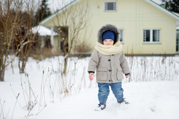 Adorable toddler boy having fun in a backyard on snowy winter day. Cute child wearing warm clothes playing in a snow.