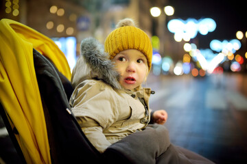 Cute toddler boy having fun on Christmas time in Vilnius, Lithuania. Small child in a stroller on Christmas market.