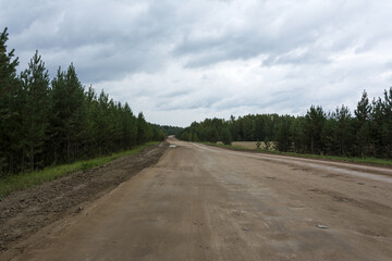 Fototapeta na wymiar Dirt road made of clay surrounded by coniferous forest