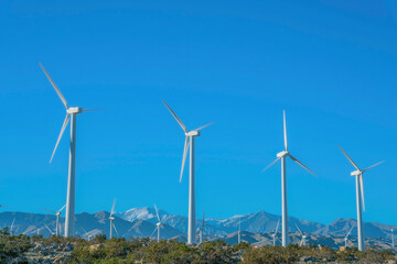 Fototapeta premium Windmills with three sharp blades against mountains and blue sky background