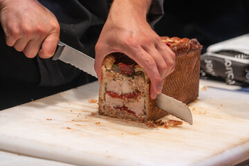 Male hand slicing with a big knife a pate en croute an appetizer  meat pie wrapped in hot water crust pastry at a French market. - obrazy, fototapety, plakaty